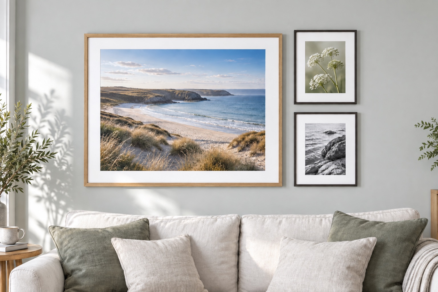 A large wooden picture frame displaying a coastal print above a sofa, alongside two smaller framed photographs