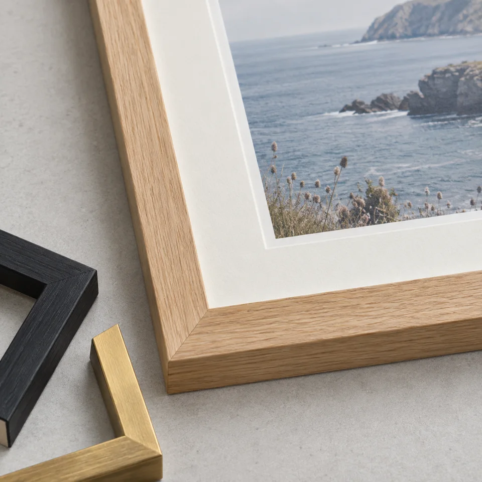 Close-up of a wood frame’s mitred corner and bevelled white mount, beside black and gold finish samples