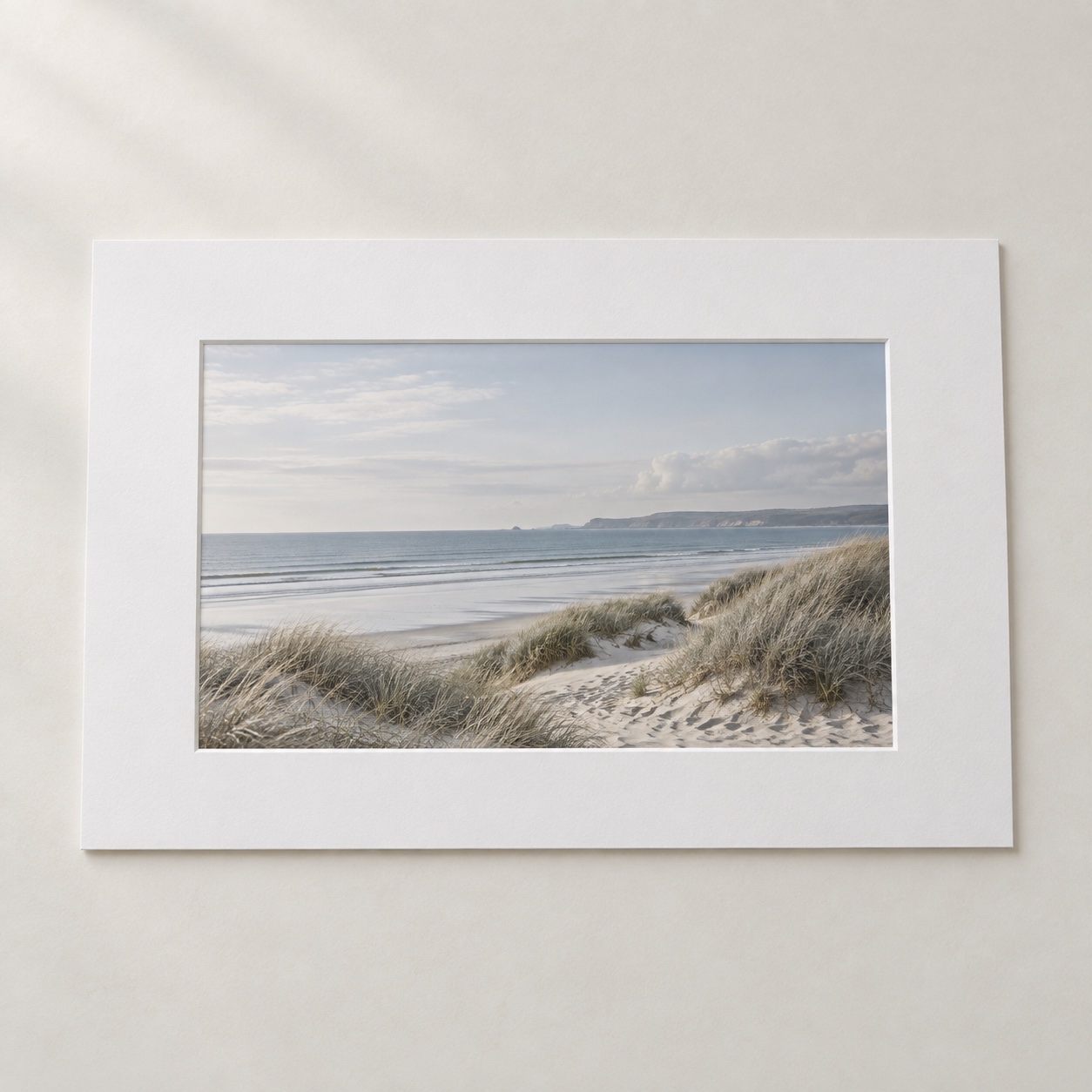 A coastal photograph in a single warm-white picture mount on a neutral tabletop